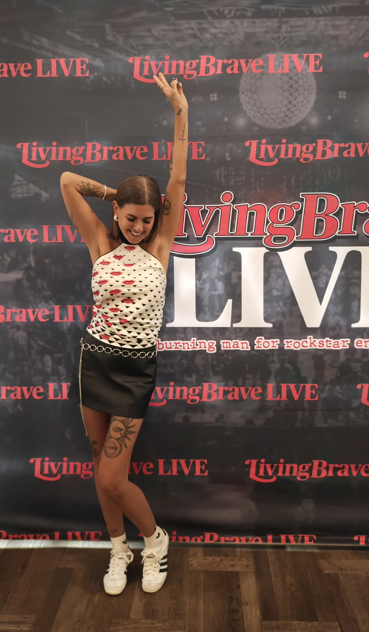Cortnie with arms raised in front of a wall covered in the words Living Brave LIVE